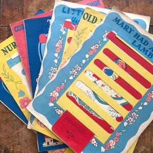 May include: A collection of vintage children's storybooks with interactive sliding panels. The covers feature colorful illustrations, floral borders, and titles including Mary Had A Lamb, Little Old Woman, and Nursery Rhymes, with text reading Billy Move.