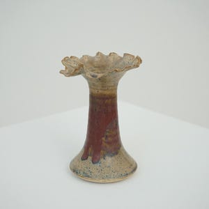 Può includere: Un vaso in ceramica con la parte superiore a balze e una base svasata. Il vaso presenta una sfumatura di colore, che passa da una parte superiore beige a una sezione centrale rosso intenso e una base maculata. È un oggetto decorativo.