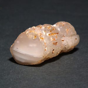 May include: A translucent, light-colored stone with a rounded shape and a textured surface. The stone has areas of white and brown coloration. The object is set against a dark background.