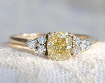 May include: A gold and silver ring featuring a large, cushion-cut yellow diamond as the centerpiece. The ring is flanked by smaller, round white diamonds on each side, set against a white background.