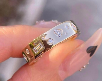 Puede incluir: Un anillo de banda de oro con una variedad de pequeños diamantes engastados en diferentes formas, incluyendo redonda, cuadrada y triangular.