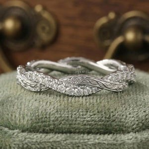 May include: A silver-toned band ring featuring a twisted design with one strand encrusted with small clear stones and the other strand displaying intricate engraved floral patterns. The word INFIORMIA is etched in small letters on the metal surface.