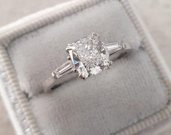 May include: A silver ring with a large, cushion-cut diamond center stone and two smaller baguette-cut diamonds on either side.