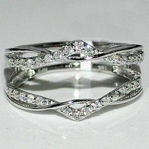 May include: A silver ring with a double band design. The bands are intertwined and set with small, clear stones. The ring is a delicate and elegant piece of jewellery.