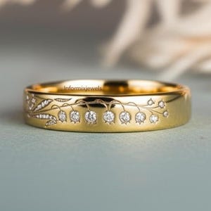 Op de afbeelding: Een gouden ring met een bloemmotief. De ring heeft een band met een reeks kleine, ronde diamanten in een bloemmotief. De ring heeft de tekst "Informixjewels" gegraveerd op de zijkant.