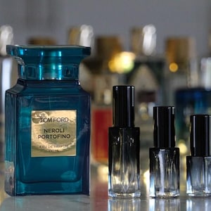 May include: A large rectangular teal glass perfume bottle with a gold label reading TOM FORD NEROLI PORTOFINO EAU DE PARFUM 100 ML, positioned next to three smaller, clear glass cylindrical perfume sample vials with black caps.