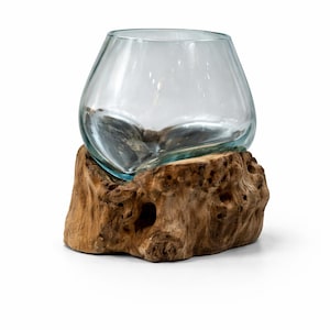 May include: A clear glass bowl with a rounded shape sits atop a natural, textured wooden base. The wood has a warm brown color with visible knots and holes, creating a rustic aesthetic. The bowl appears to be empty.