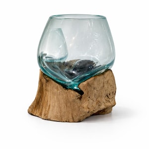 May include: A clear glass bowl with a unique shape, resting on a natural wood base. The bowl has a small, integrated glass element inside. The wood base is a light brown color.