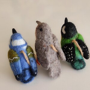 May include: Three felt bird ornaments, each with a different colour and pattern. The birds are blue, grey, and green with black accents. They are all tied together with twine.