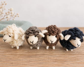 May include: Four small sheep figurines crafted from yarn and felt. Each sheep features a cream-colored felt face with black stitched eyes and a nose, paired with a textured, looped yarn body in cream, gray, brown, and dark navy blue colors.