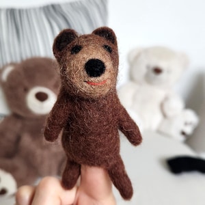 Op de afbeelding: Een bruine vingerpop van vilt in de vorm van een beer met zwarte ogen en een rode mond.