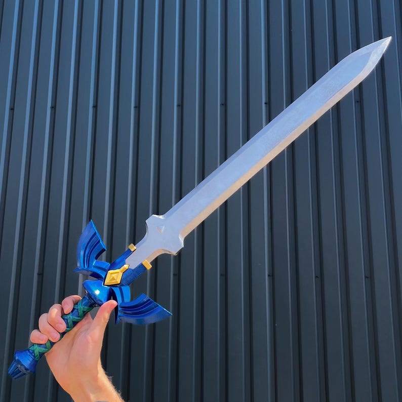 May include: A silver-colored sword with a blue and gold hilt. The blade is long and pointed, and the hilt features a stylized design with blue wings. The handle is blue and green. The sword is held against a dark gray background.