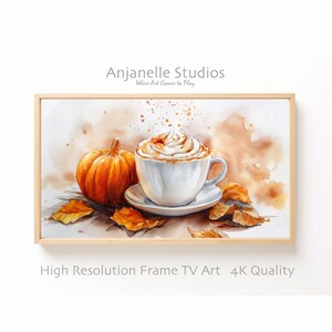 Peut inclure: Peinture à l'aquarelle d'une citrouille, d'une tasse à café blanche avec de la crème fouettée et des feuilles d'automne. L'œuvre est encadrée dans un cadre en bois clair. Le texte "Anjanelle Studios" et "High Resolution Frame TV Art 4K Quality" sont visibles.