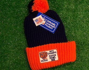 May include: A blue and orange knit beanie with a pom pom on top. The beanie has a patch that says "NFC Champs Super Bowl XX Bears". The beanie also has a tag that says "Officially Licensed Product".