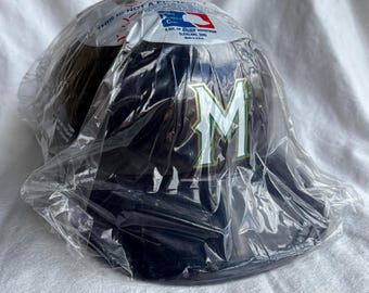 May include: A navy blue baseball cap with a white and green "M" logo. The cap is in a clear plastic bag. The packaging has text and a Major League Baseball logo.
