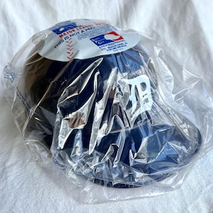Op de afbeelding: Een marineblauwe baseballcap met het witte logo van de Detroit Tigers, verpakt in doorzichtig plastic. De cap heeft een gebogen klep en een gestructureerde kroon. De verpakking bevat een label met de tekst "MAJOR LEAGUE BASEBALL".