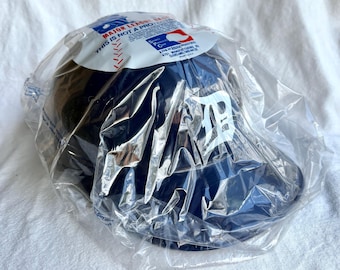 May include: A navy blue baseball cap with the Detroit Tigers logo in white, packaged in clear plastic. The cap has a curved brim and a structured crown. The packaging includes a label with text that reads "MAJOR LEAGUE BASEBALL" and "THIS IS NOT A PRO PRODUCT".
