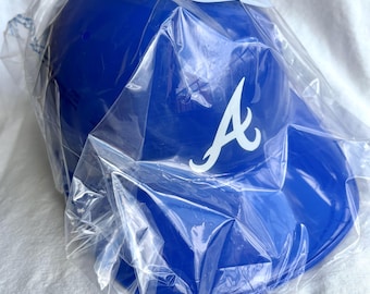 May include: A blue baseball cap with a white "A" logo, packaged in clear plastic. The cap has a curved brim and is likely new. The packaging has text that is partially visible. The cap is a sports-themed item.