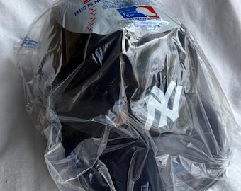 May include: A black baseball cap with the New York Yankees logo in white, packaged in clear plastic. The packaging includes text and a Major League Baseball logo.