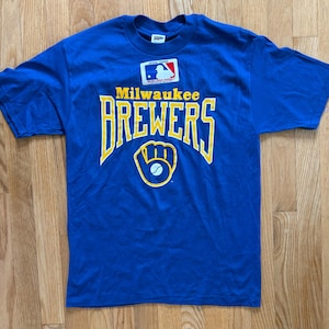 May include: A blue t-shirt with the words "Milwaukee Brewers" in yellow lettering and a yellow baseball glove with a white baseball. The shirt has a small tag with the Major League Baseball logo.