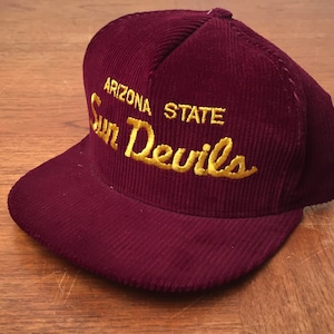 May include: A maroon corduroy baseball cap with a gold embroidered logo that reads "Arizona State Sun Devils".