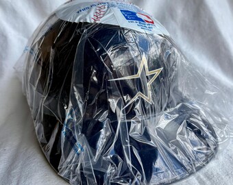 May include: A navy blue baseball cap with a gold star logo, packaged in clear plastic. The cap has a curved brim and is likely new. The packaging includes text and a baseball graphic.