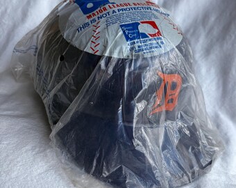 May include: A navy blue baseball helmet in a clear plastic bag. The helmet has an orange "D" logo and is labeled "Major League Baseball." The packaging includes the text "This is not a protective helmet."