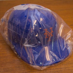 Puede incluir: Una gorra de b&eacute;isbol azul con el logotipo de los New York Yankees en naranja. La gorra est&aacute; empaquetada en una bolsa de pl&aacute;stico transparente.