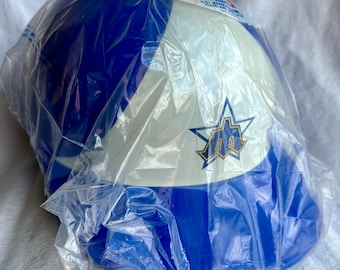 May include: A blue and white baseball cap with a team logo in a plastic wrapper. The cap has a blue crown and a white front panel with a logo. The plastic wrapper is clear.