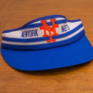 Puede incluir: Una visera a rayas azul y blanca con el logotipo de los Mets de Nueva York y "NEW YORK METS" bordado en naranja.