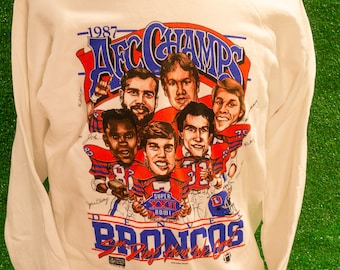 May include: White long-sleeve sweatshirt with a blue, red, and white graphic of the 1987 Denver Broncos AFC Champions team. The graphic includes the team's logo, the text "AFC Champs", and the text "Super Bowl XXII".