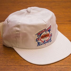 Pu&ograve; includere: Cappellino da baseball bianco con una toppa blu, rossa e bianca che dice "World Series '79 Giants NL Champs".