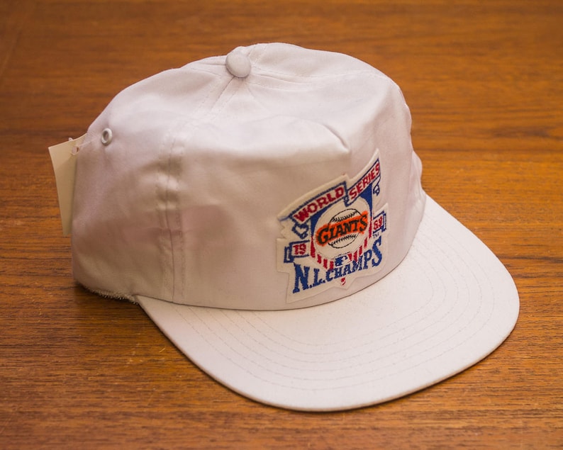 Pu&ograve; includere: Cappellino da baseball bianco con una toppa blu, rossa e bianca che dice "World Series '79 Giants NL Champs".