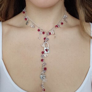May include: A silver necklace with a long pendant chain featuring red and clear beads, small silver hearts, keys, and lock charms. The pendant lock has the word "LOVE" engraved on it.