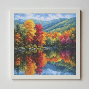 Könnte beinhalten: Eine quadratisch gerahmte Kreuzstichstickerei, die eine lebendige Herbstlandschaft mit gelben, orangen und roten Bäumen an einem ruhigen See zeigt. Die Szene enthält eine Spiegelung des farbenfrohen Waldes im Wasser und blaue Berge im Hintergrund.