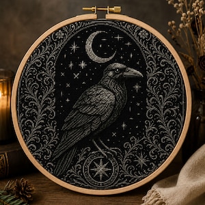May include: A circular wooden embroidery hoop containing a black fabric piece with a cross-stitched design of a raven perched above a star emblem. The scene features a crescent moon and small stars against a dark background, framed by intricate silver-toned floral scrollwork borders.