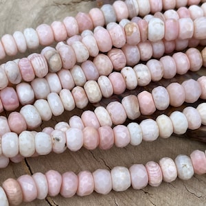 May include: A strand of pink opal beads with a faceted, rounded shape. The beads are strung on a clear thread and are ready to be used for jewelry making.
