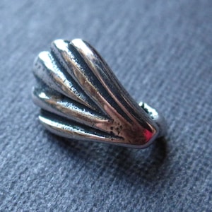 May include: A silver charm in the shape of a fan with a textured surface.
