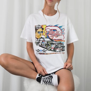 May include: White t-shirt with a vintage-style graphic of a race car driver and a race car. The graphic includes the text "Dale Earnhardt Jr."