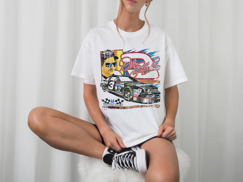 May include: White t-shirt with a vintage-style graphic of a race car driver and a race car. The graphic includes the text "Dale Earnhardt Jr."