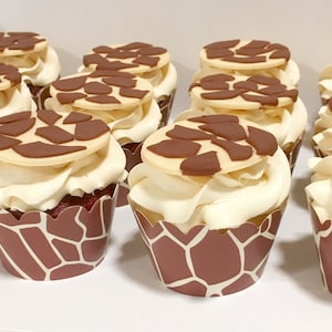 May include: A close-up of nine cupcakes decorated with brown and beige frosting and a brown and beige giraffe print. The cupcakes are arranged in a row on a white surface.
