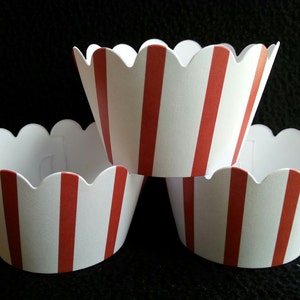 May include: Three white cupcake liners with red stripes. The liners are scalloped and have a wavy edge.