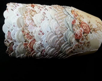 May include: A stack of cupcake liners with a floral pattern in shades of pink, brown, and white. The liners have a scalloped edge.
