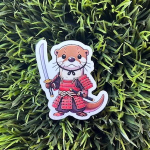 May include: A cartoon otter wearing red and black samurai armor and holding a sword. The otter is standing on a green grassy background.