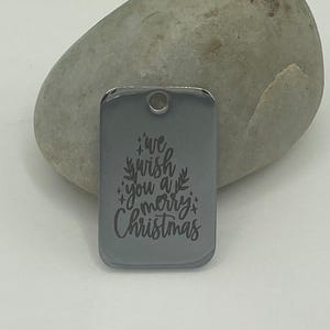 May include: A silver metal tag with a Christmas tree design and the text "We wish you a merry Christmas".