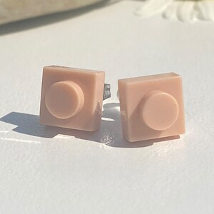 May include: A pair of pink Lego-inspired stud earrings. The earrings are square shaped with a round center.
