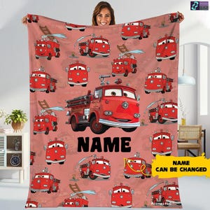 A woman is holding up a blanket with a repeating pattern of red fire trucks and the word "NAME" printed on it.