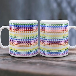 May include: Two white ceramic mugs with a rainbow design. The design features horizontal bands of text in various colors, including red, orange, yellow, green, blue, and purple. The text reads "DONALD TRUMP" repeatedly.