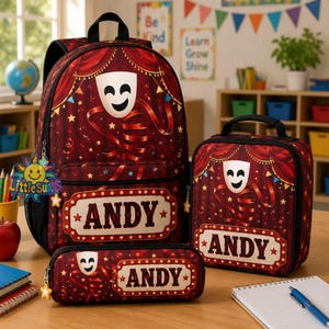 May include: A backpack, lunch bag, and pencil case set in a dark red theater curtain theme. Each item features a white comedy mask, gold stars, and a marquee-style sign with the name ANDY printed in bold, dark lettering on a cream background.