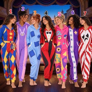 Op de afbeelding: Zeven jumpsuits met rits en capuchon met verschillende patronen: een blauw, rood en geel ruitpatroon, een paars konijnontwerp, een lichtblauwe patchworkstijl, een rode smokinglook, een roze geometrische print, een paars oogpatroon en rode strepen.